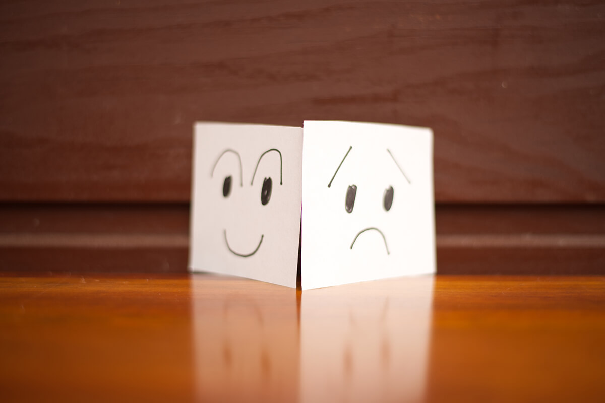 Symbolbild für Lob und Beschwerde: Zeichnungen eines lachenden und eines traurigen Gesichts auf zwei Blättern, Fotocredit iStock.com / Asobinin Zeichnungen eines lachenden und eines traurigen Gesichts