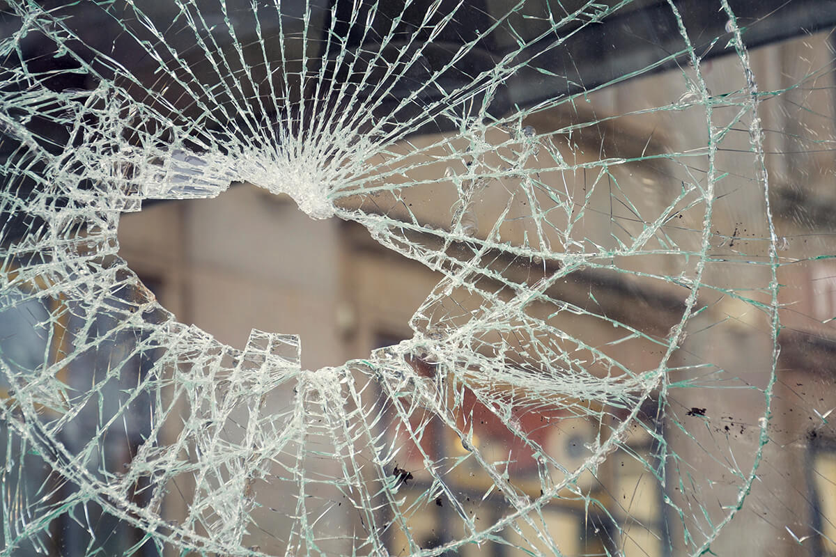 Symbolbild für Sachbeschädigung: Großes Loch und viele Glassprünge in einer beschädigten Glasscheibe, Fotocredit iStock.com / josefkubes Beschädigte Glasscheibe