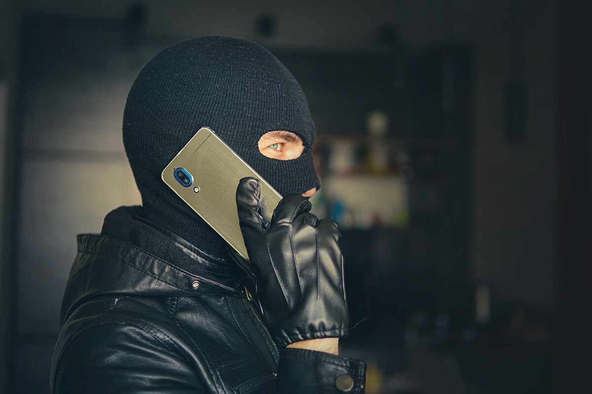 Person mit schwarzer Gesichtsmaske und Mobiltelefon